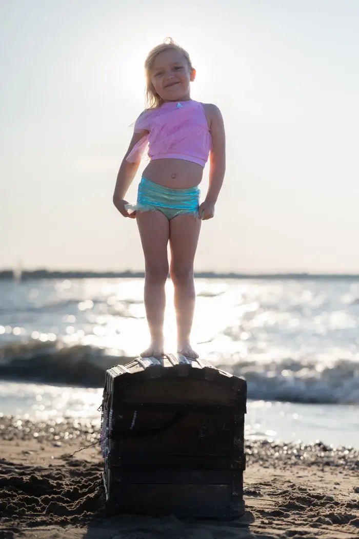 girl stood on rock on beach wearing mermaid costume