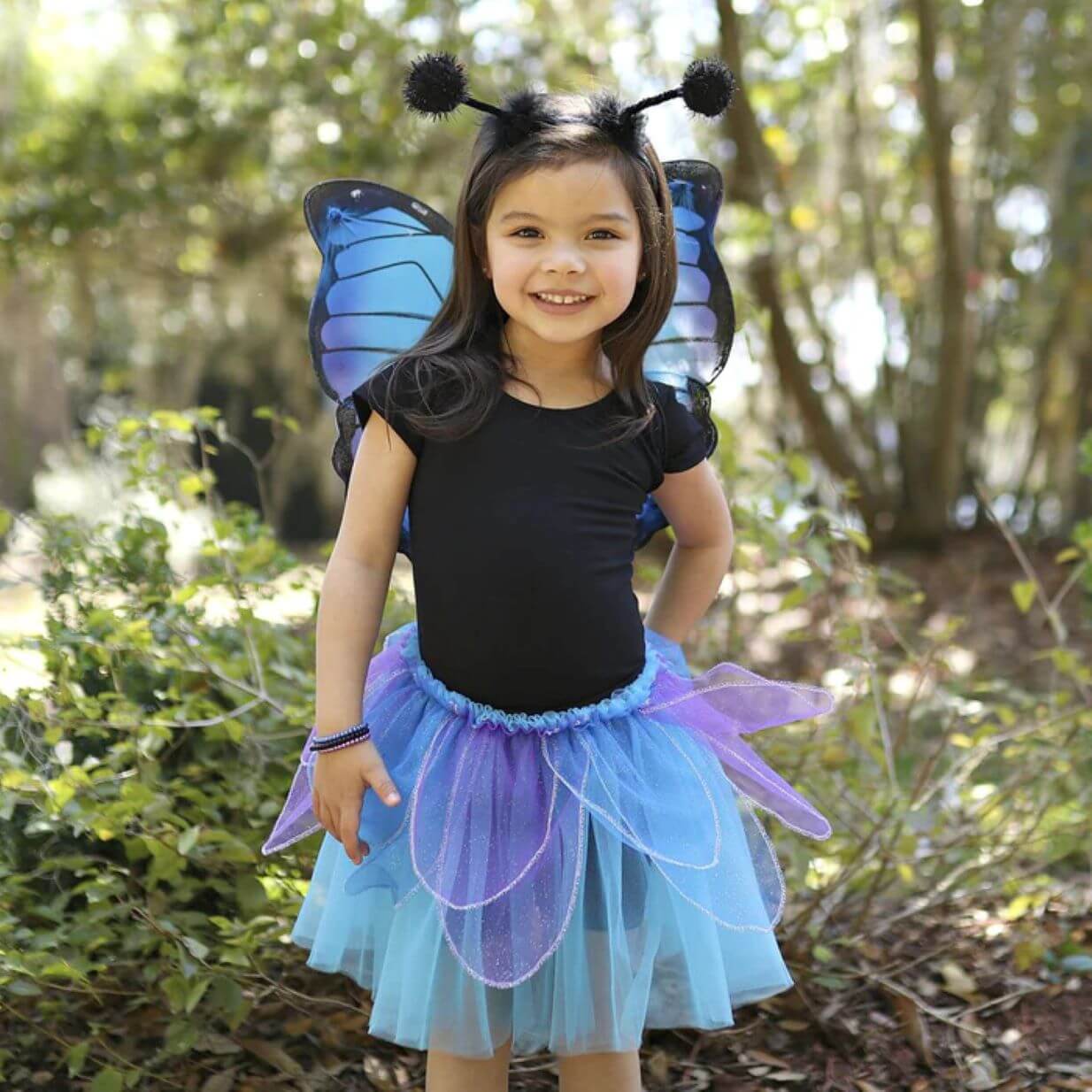 young girl in black top with blue and purple petal tutu skirt, blue and purple butterfly wings and black headband with butterfly antenna