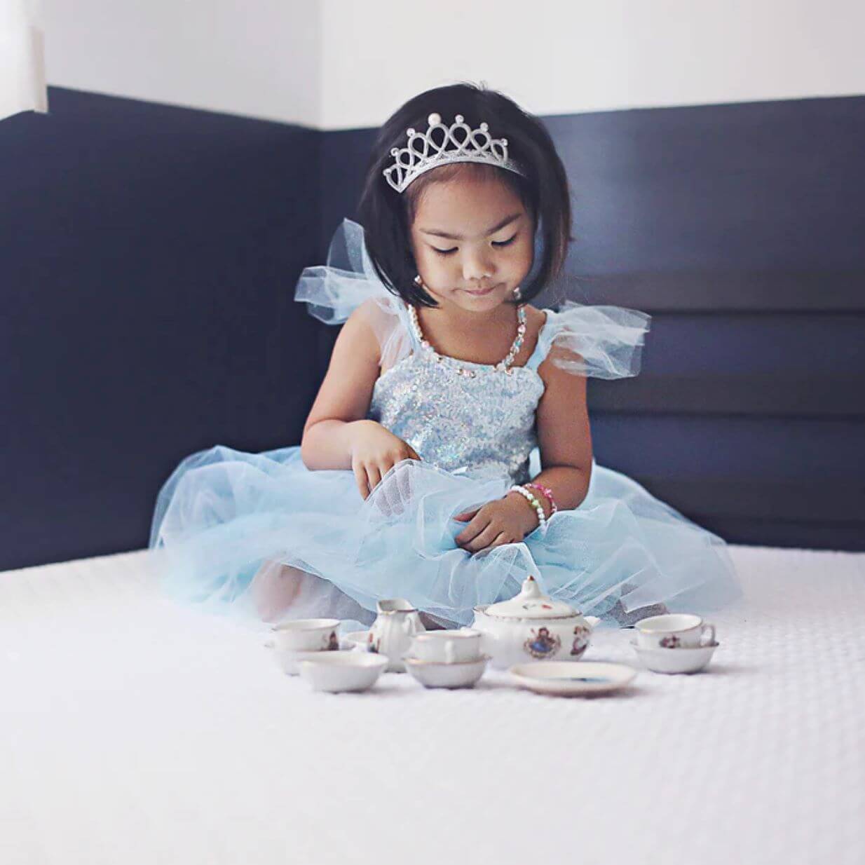Small girl in blue sequinned party dress with silver tiara and play tea set