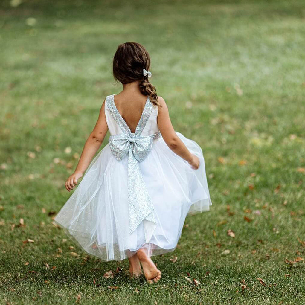 Girl in a park in silver flower girl dress with sequin bow