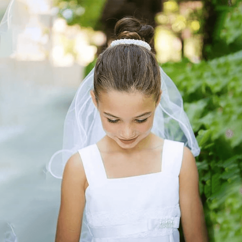 Girls in white flower girl dress wearing a pearl bun veil