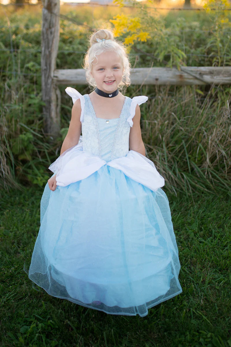 Young girl in a light blue dress with white gloves sitting on grass.