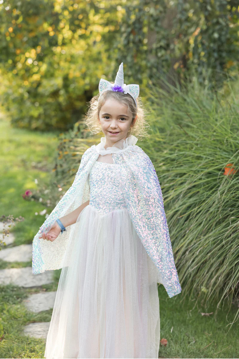 Young girl in a unicorn costume with a white dress and cape outdoors.