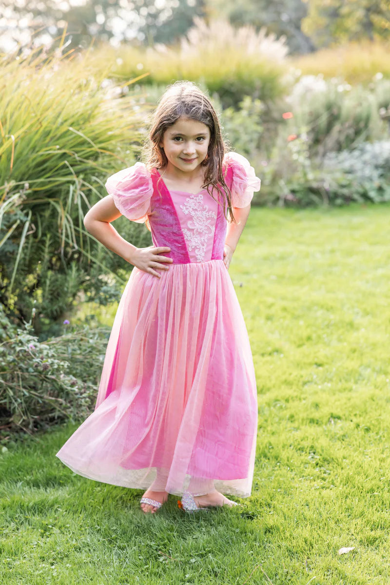 Young girl in a pink dress standing on grass with greenery in the background