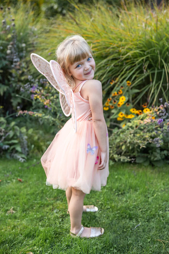 Young girl in a fairy costume standing outdoors with greenery and flowers in the background
