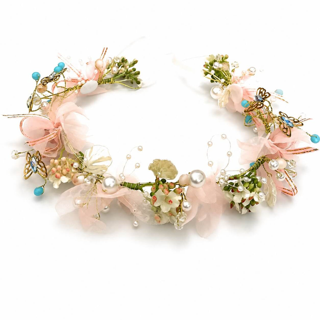 A delicate floral headband with pink tulle, artificial flowers, green leaves, and white pearls on a white background.