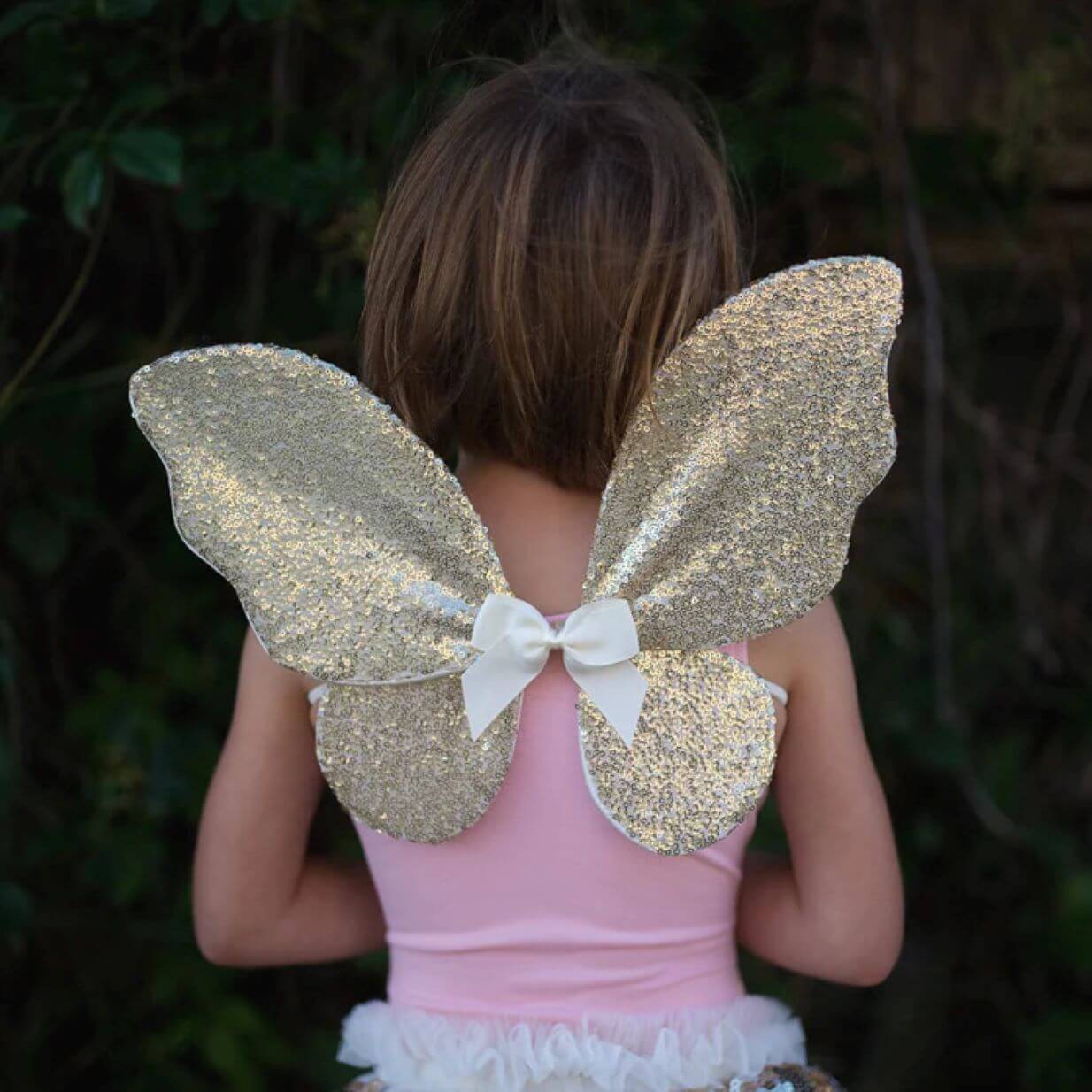 back view of young girl in pink top wearing gold sequin fairy wings