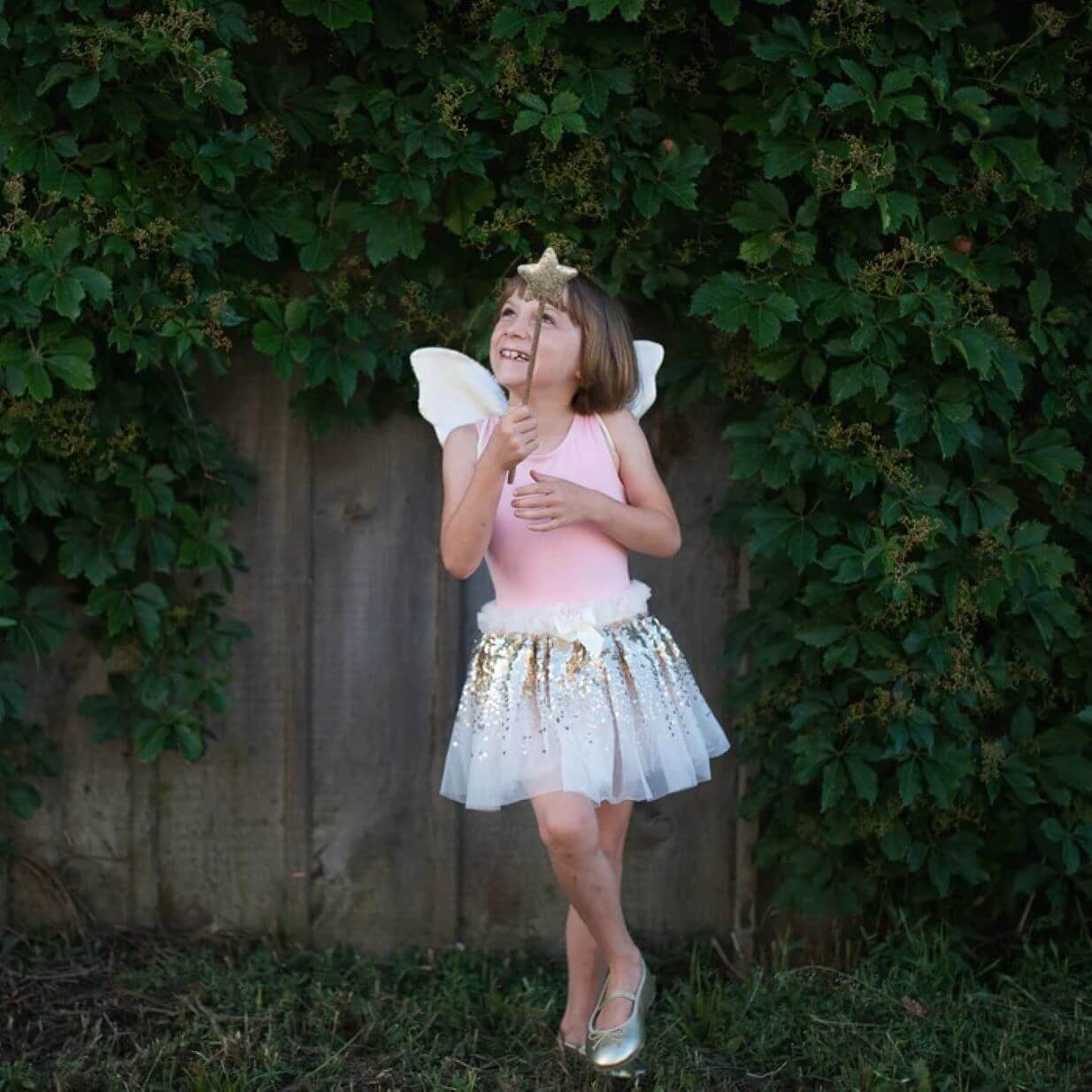 young girl in white and gold tutu skirt with white and gold wings with gold sequin wand