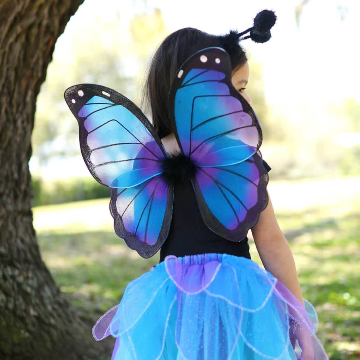 Back view of young girl wearing blue purple and black butterfly wings with a blue and purple petal tutu skirt