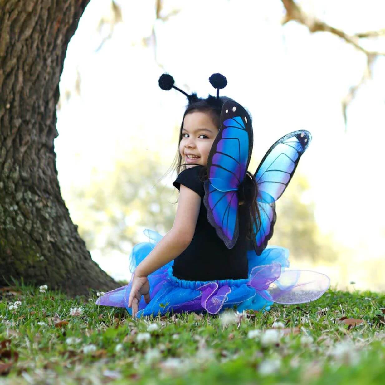 Small girl sitting wearing blue and purple butterfly wings with antenna headset