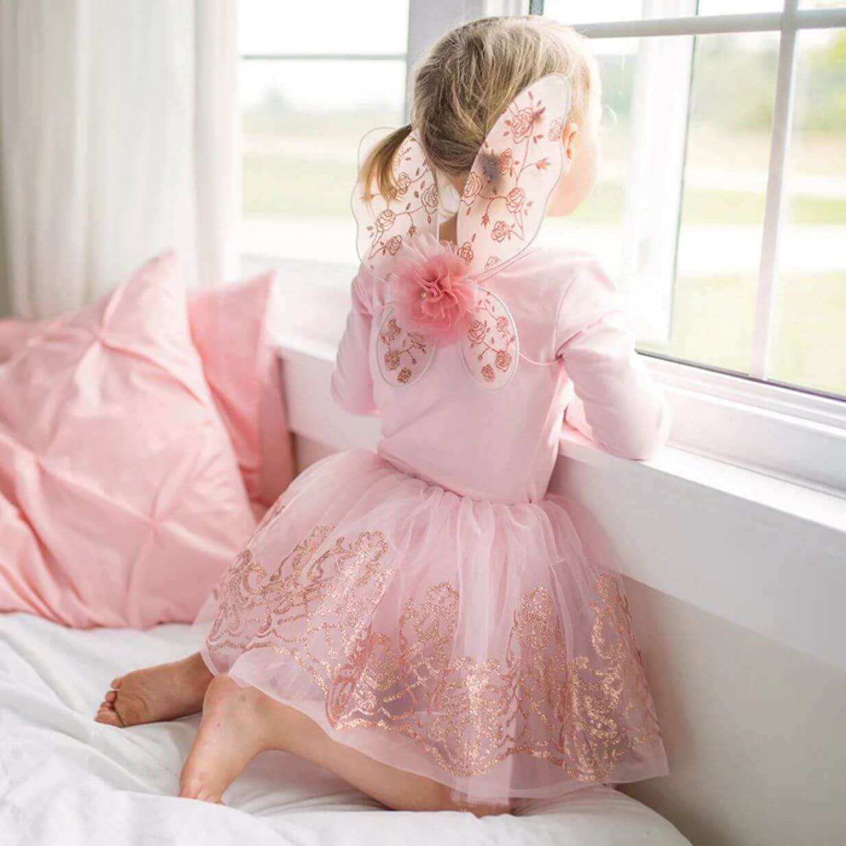 picture of young girl looking out of the window wearing a pink fairy skirt and matching wings