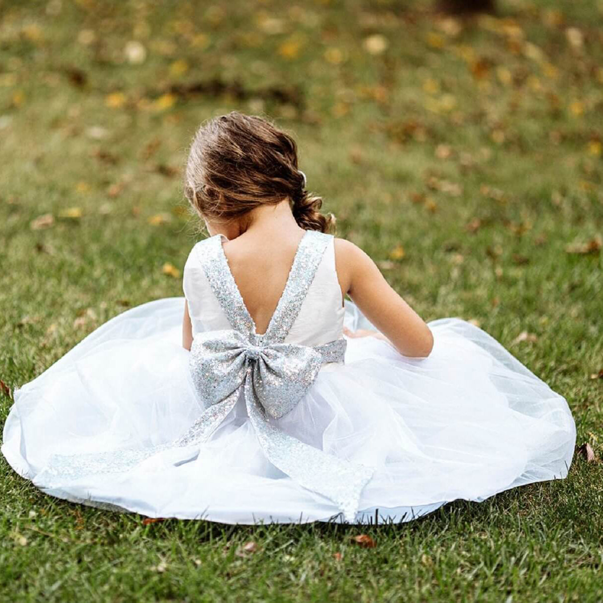 Girl sitting on grass in silver flower girl dress