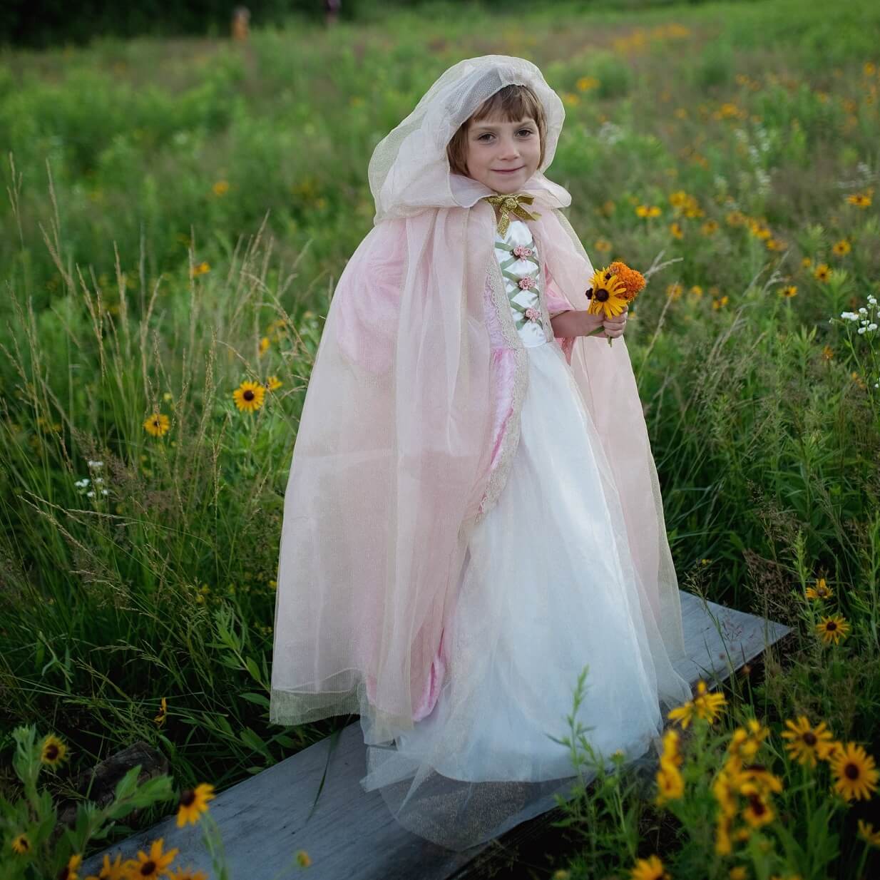 Girl wearing a pink and gold princess cape with the hood up in a field